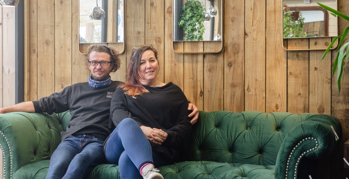Couple sat on a green velvet sofa in a garden centre