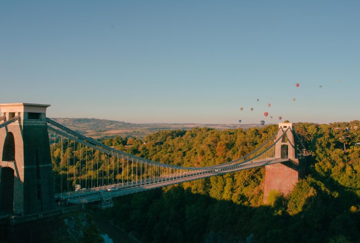 Suspension bridge in the foreground with hot air balloons flying in the distance