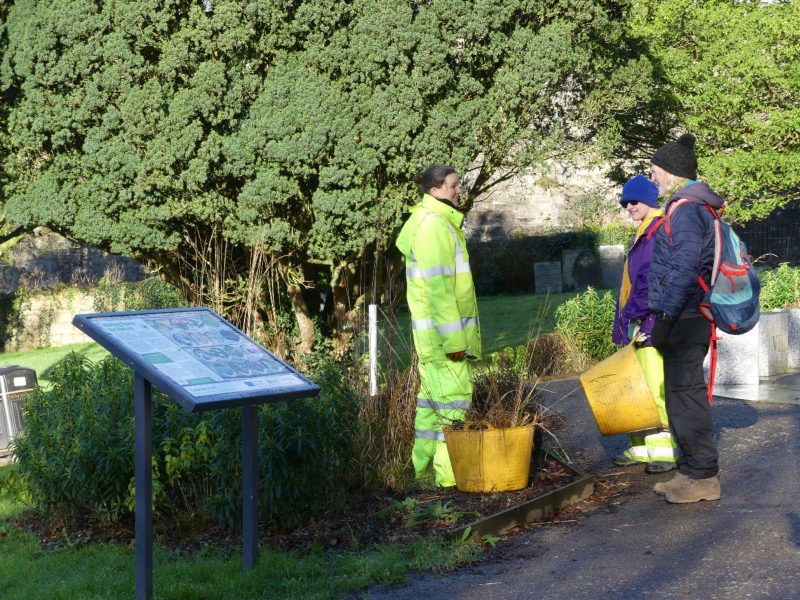 Garden worker in a park wearing high-vis speaking with two people in